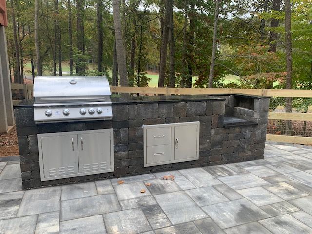 Outdoor stone patio with built-in grill, storage cabinets, and side shelf.