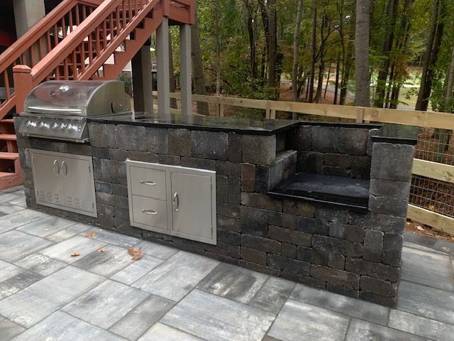 Outdoor stone barbecue grill with stainless steel doors and a built-in side bench on a patio