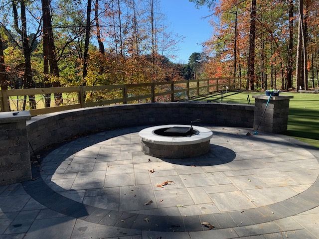 Circular stone fire pit in a wooded park overlook with autumn trees and a wooden railing