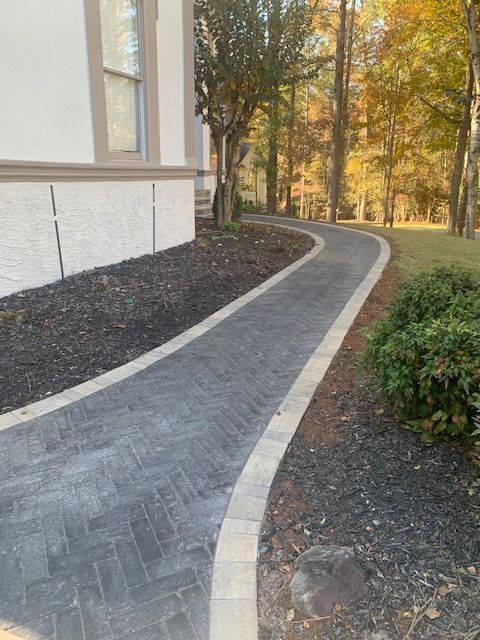 Curving brick walkway beside a house with autumn trees and mulch beds