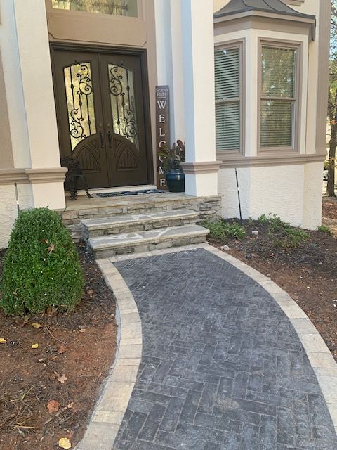 Curved brick walkway leading to a front door with steps and landscaped shrubs