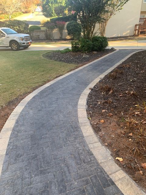 Curved gray walkway with light edging beside a landscaped yard and parked car