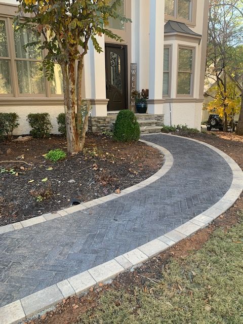 Curved stone walkway leading to a house entrance with trees and landscaping