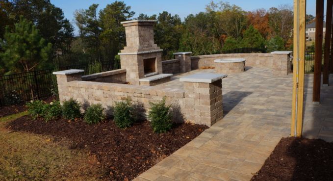 Stone patio with low brick walls and a central fireplace in a landscaped yard