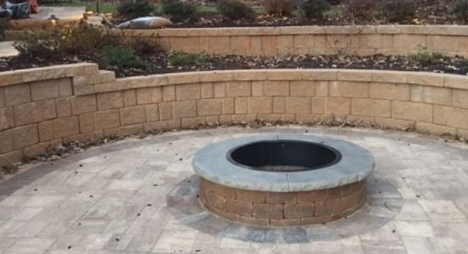Stone fire pit centered on a paved patio with a curved retaining wall behind it