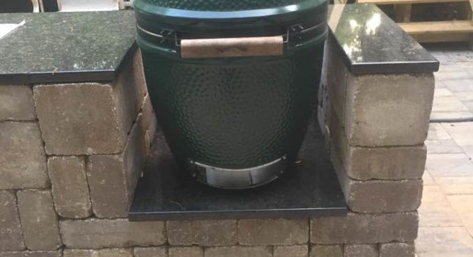 Green ceramic grill set into a brick outdoor counter, with a silver handle and black base.