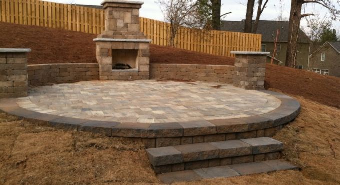Stone patio with built-in brick fireplace and steps in a backyard