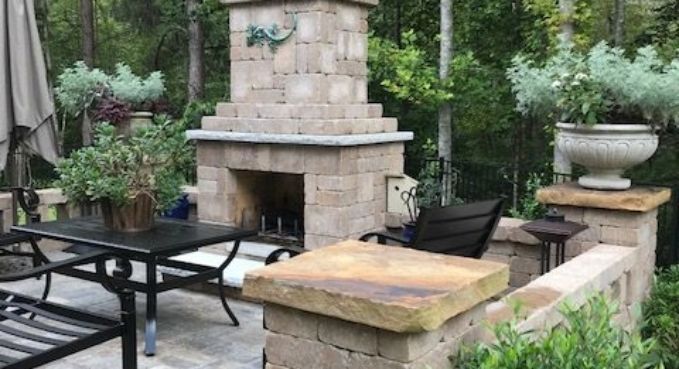 Patio with stone outdoor fireplace, black metal table, chairs, and potted greenery