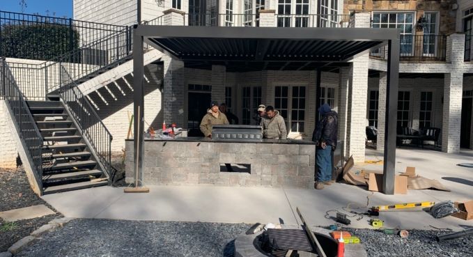 Two people sitting on a patio beside exterior stairs and a building entrance under a black awning.