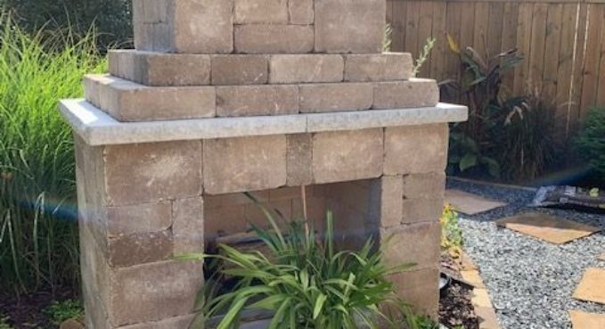 Stone outdoor fireplace in a garden, surrounded by plants and gravel path