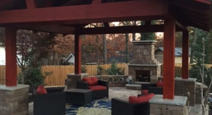 Covered outdoor patio with red beams, stone fireplace, and black chairs with red cushions