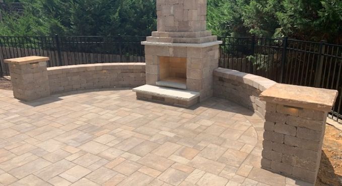 Stone patio with a central outdoor fireplace and curved seating walls overlooking trees