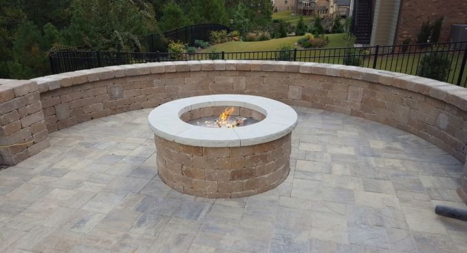 Circular stone fire pit on a paved patio with a curved retaining wall and garden beyond