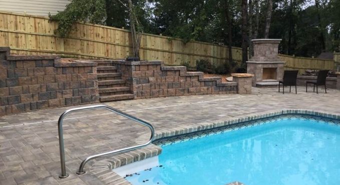 Backyard pool with metal handrail, brick patio, stone wall, and outdoor fireplace