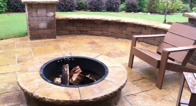 Patio fire pit with wooden chairs on a stone patio in a backyard