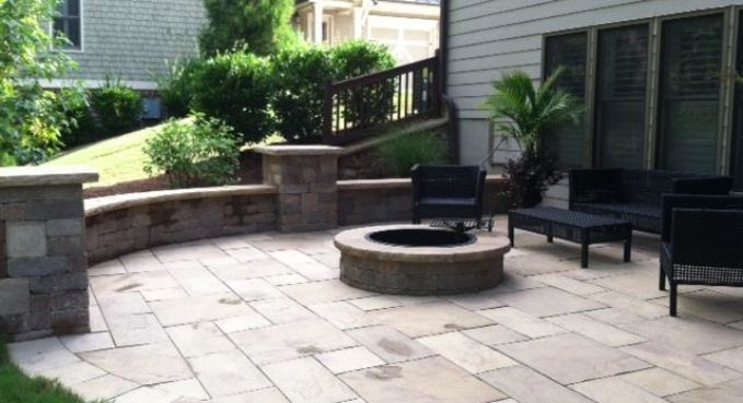 Patio with stone pavers, circular fire pit, and black outdoor chairs beside a landscaped retaining wall