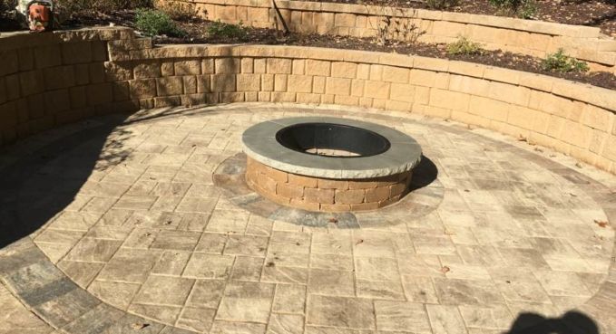 Round stone fire pit in a paved courtyard with a low curved brick wall.