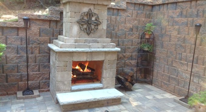 Outdoor stone fireplace with a lit fire in a brick patio courtyard