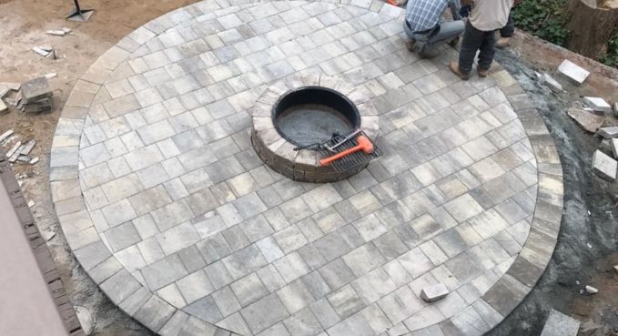 Circular stone-paved platform with a central round opening and a red tool nearby, with workers at the edge