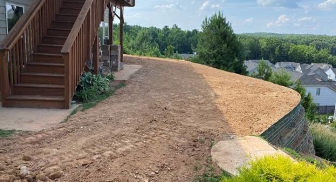 Freshly graded dirt yard beside a wooden staircase, overlooking a green suburban hillside.