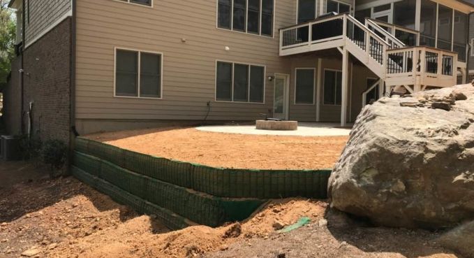 Apartment building with a small retaining wall, dirt yard, and large rocks beside an outdoor stairway.