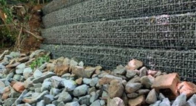Wire-mesh retaining wall with stacked rocks beside a gravel slope