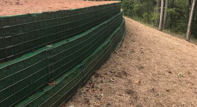 Green mesh fence along a dirt path on a sloped wooded hillside