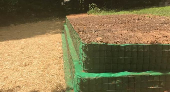 Green mesh-covered raised garden bed beside a gravel path in a sunny outdoor yard