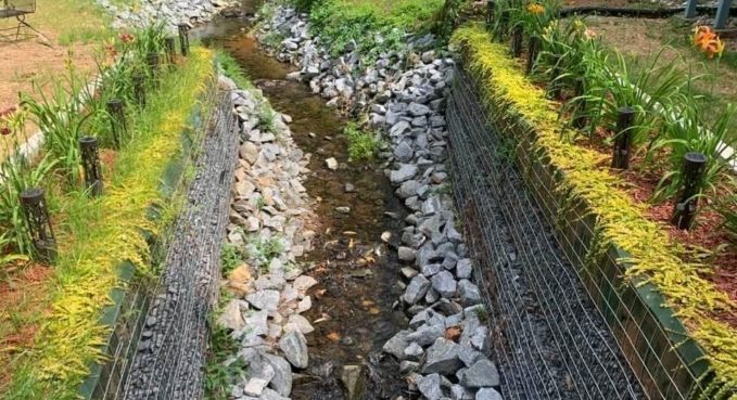 Rock-lined garden drainage trench with black mesh and rows of small plants on both sides