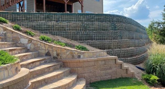 Curved stone staircase beside a wire retaining wall and landscaped hillside under a blue sky