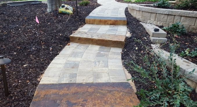 Curved stone walkway with steps in a landscaped garden, bordered by mulch and greenery.