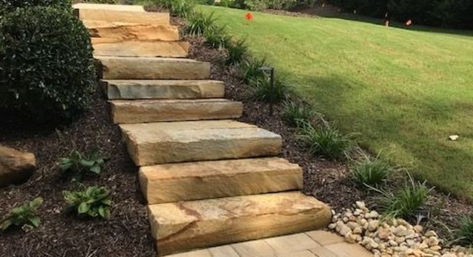 Stone steps leading up a landscaped grassy slope with mulch and small plants