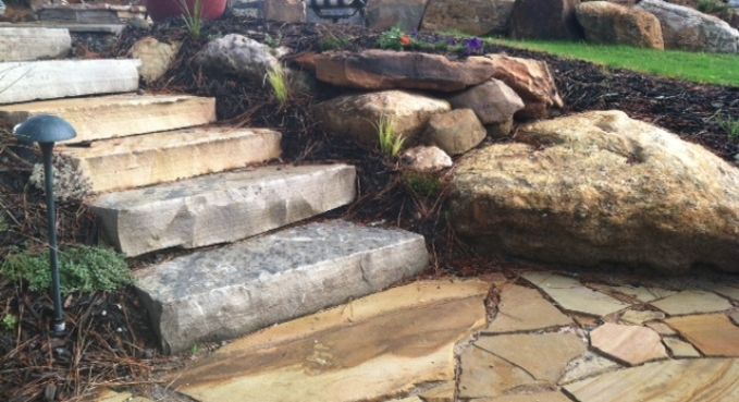 Stone garden steps beside large rocks and a paved path in a landscaped yard