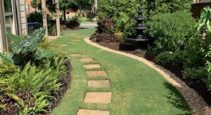 Curved stepping-stone path through a lush garden with trimmed grass and a fountain on the right