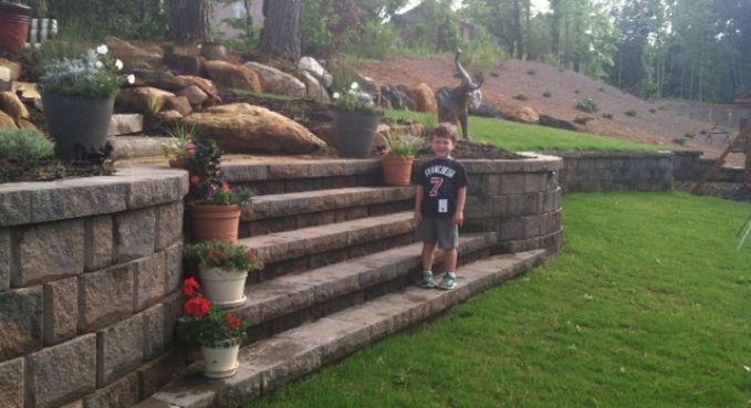 Child standing on stone steps in a landscaped garden beside a grassy lawn.