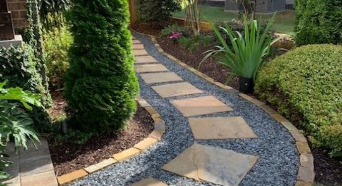 Curved garden path with stone pavers, blue gravel, and surrounding shrubs and plants