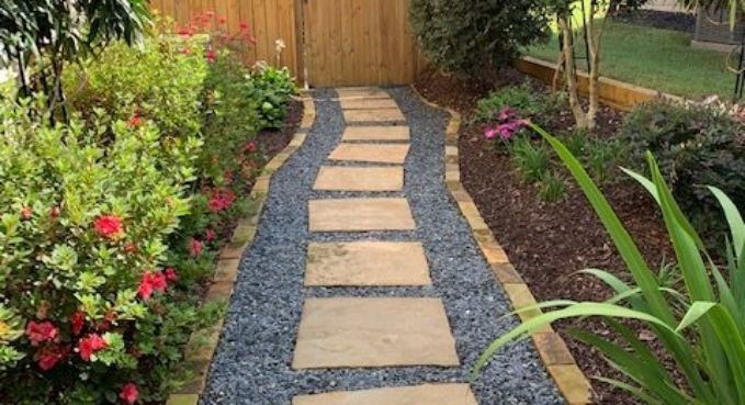 Stone stepping path through a colorful garden leading to a wooden gate and fence