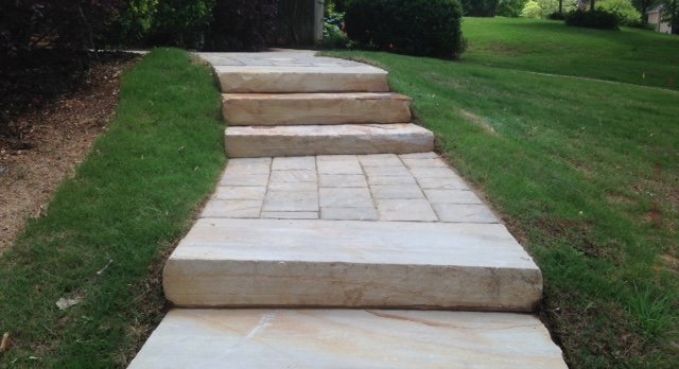 Stone steps and a paved walkway leading up a grassy slope in a garden area