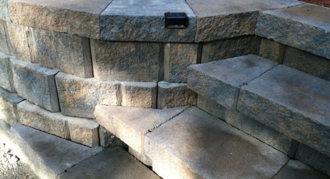 Stone steps and curved retaining wall in sunlight, with a rectangular opening at the top.