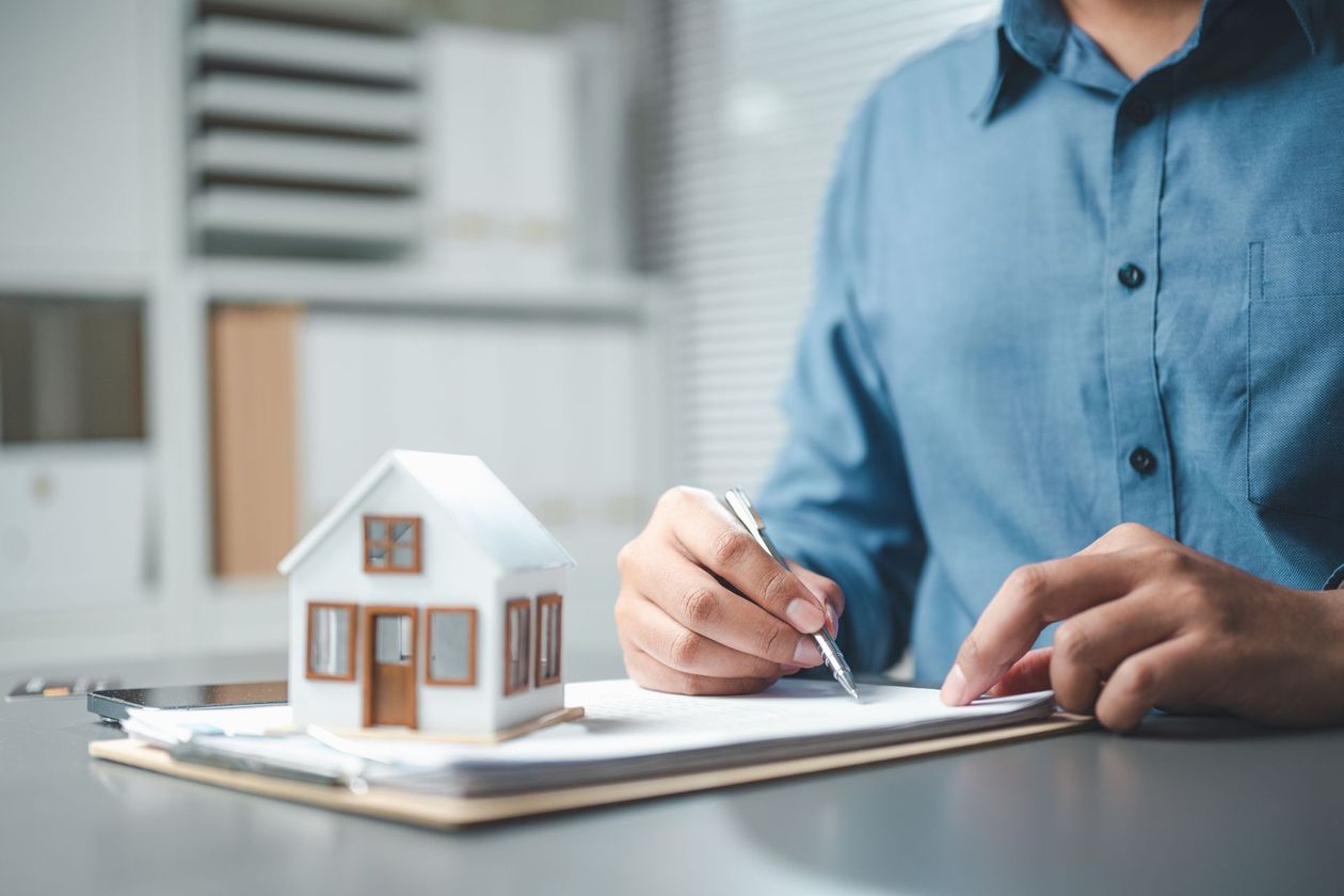 Person sketching house plans beside a small model home on a desk
