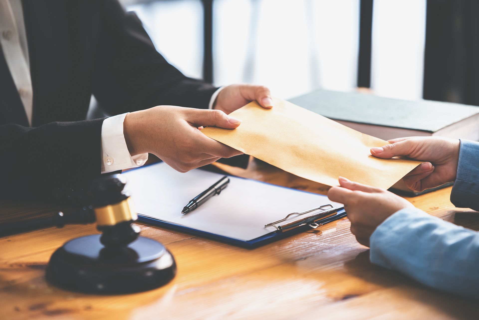 Hands exchanging a document over a desk with a gavel and clipboard during a meeting