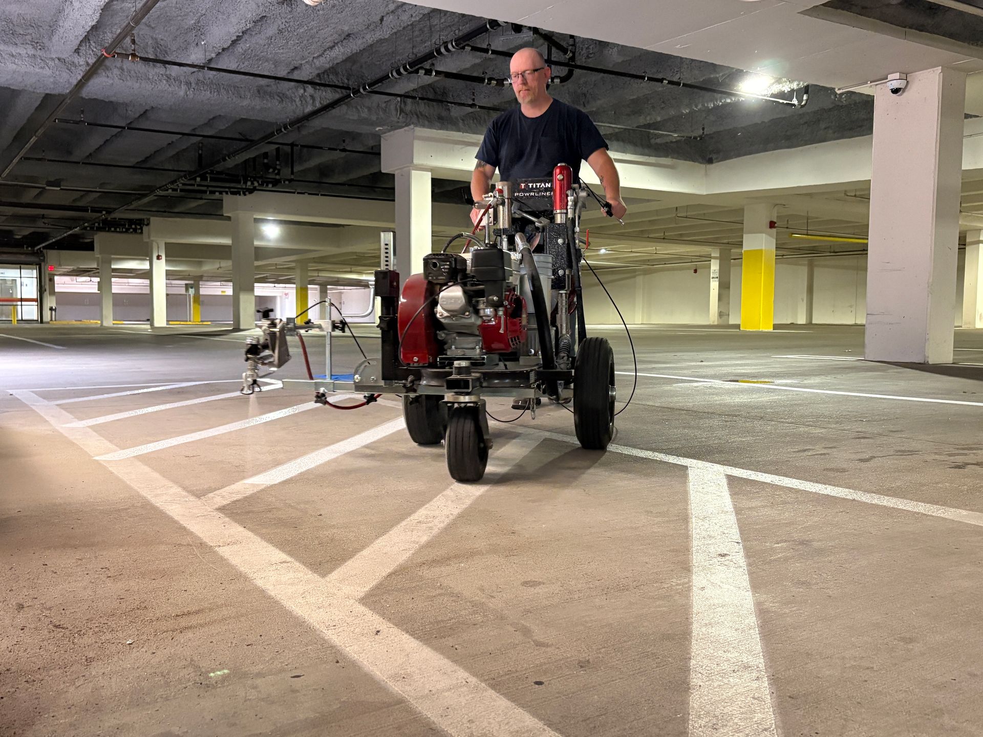 A machine marks white lines on an asphalt parking lot, with yellow numbers visible in the spaces.