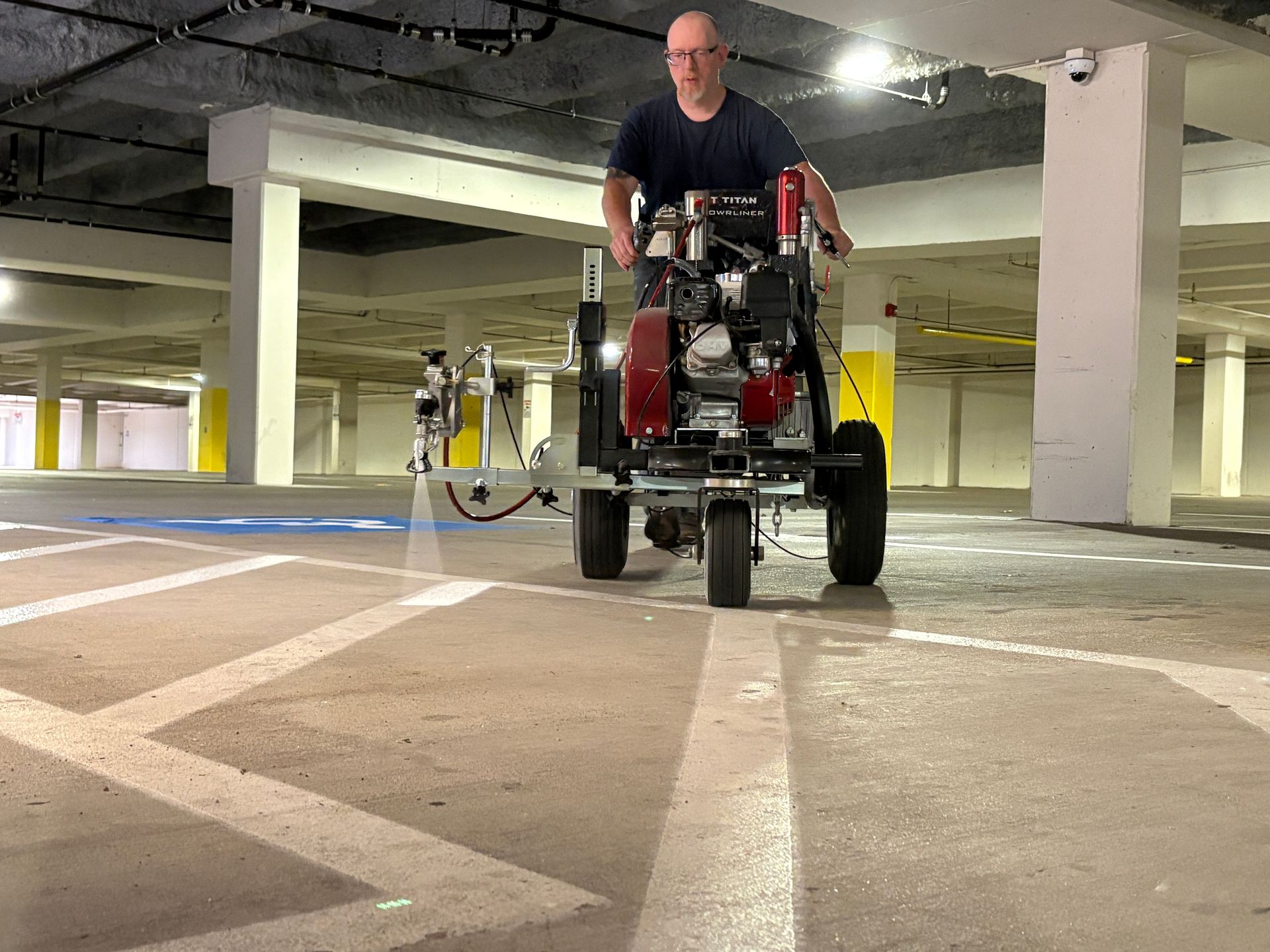 A machine sprays a fresh white line onto an asphalt road next to an existing painted line.