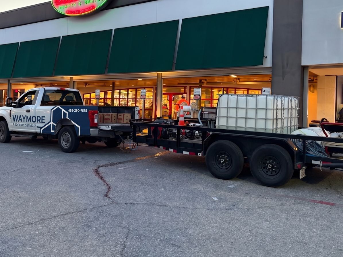 Pickup truck towing a flatbed trailer with a white water tank outside a storefront at dusk