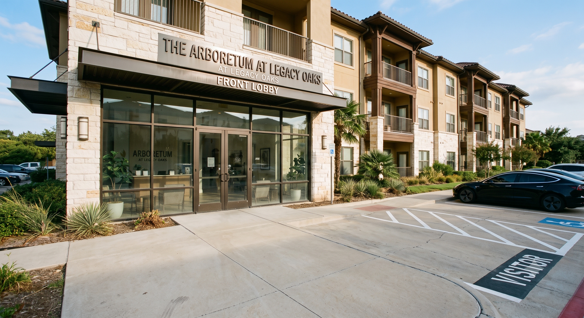 Apartment building entrance with glass doors, stone facade, and parked cars in front