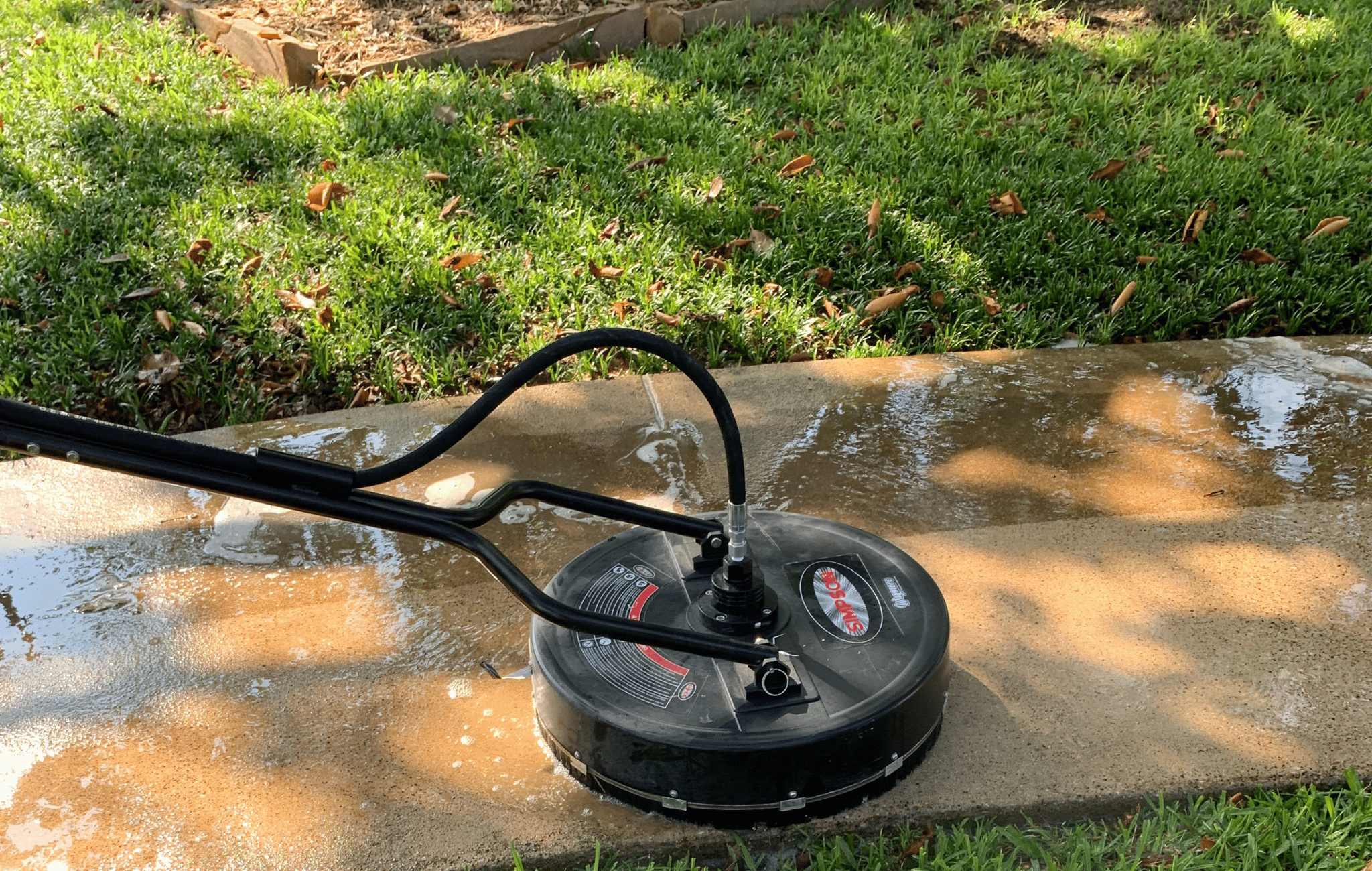 Person pushing a metal floor scrubber over a wet concrete surface indoors