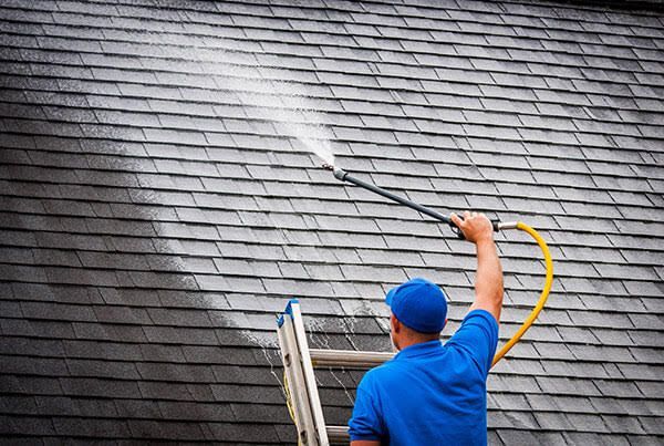 Person pushing a metal floor scrubber over a wet concrete surface indoors