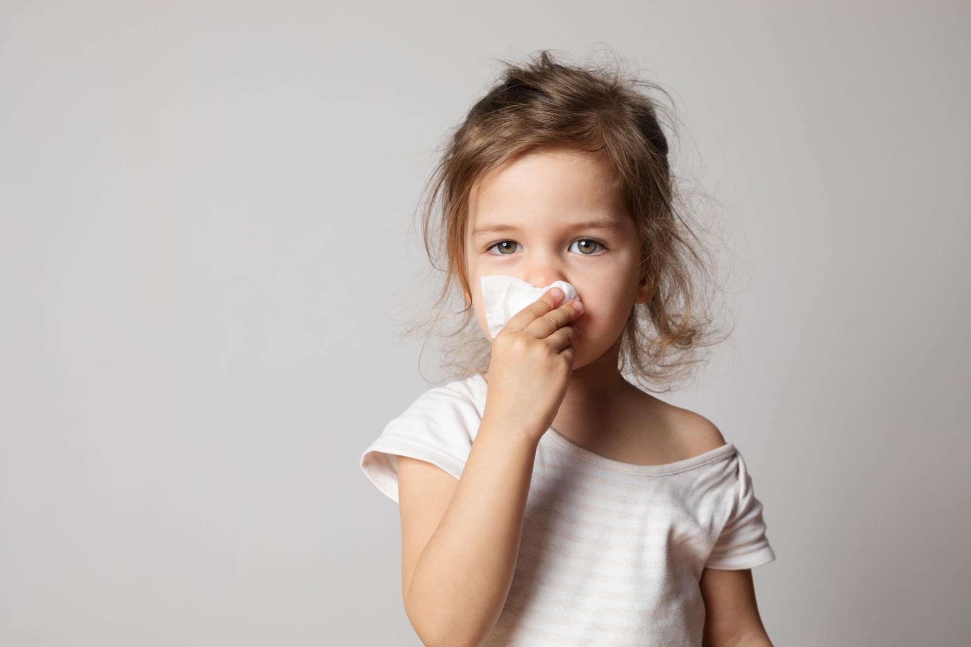 A sick girl is blowing her nose with a tissue