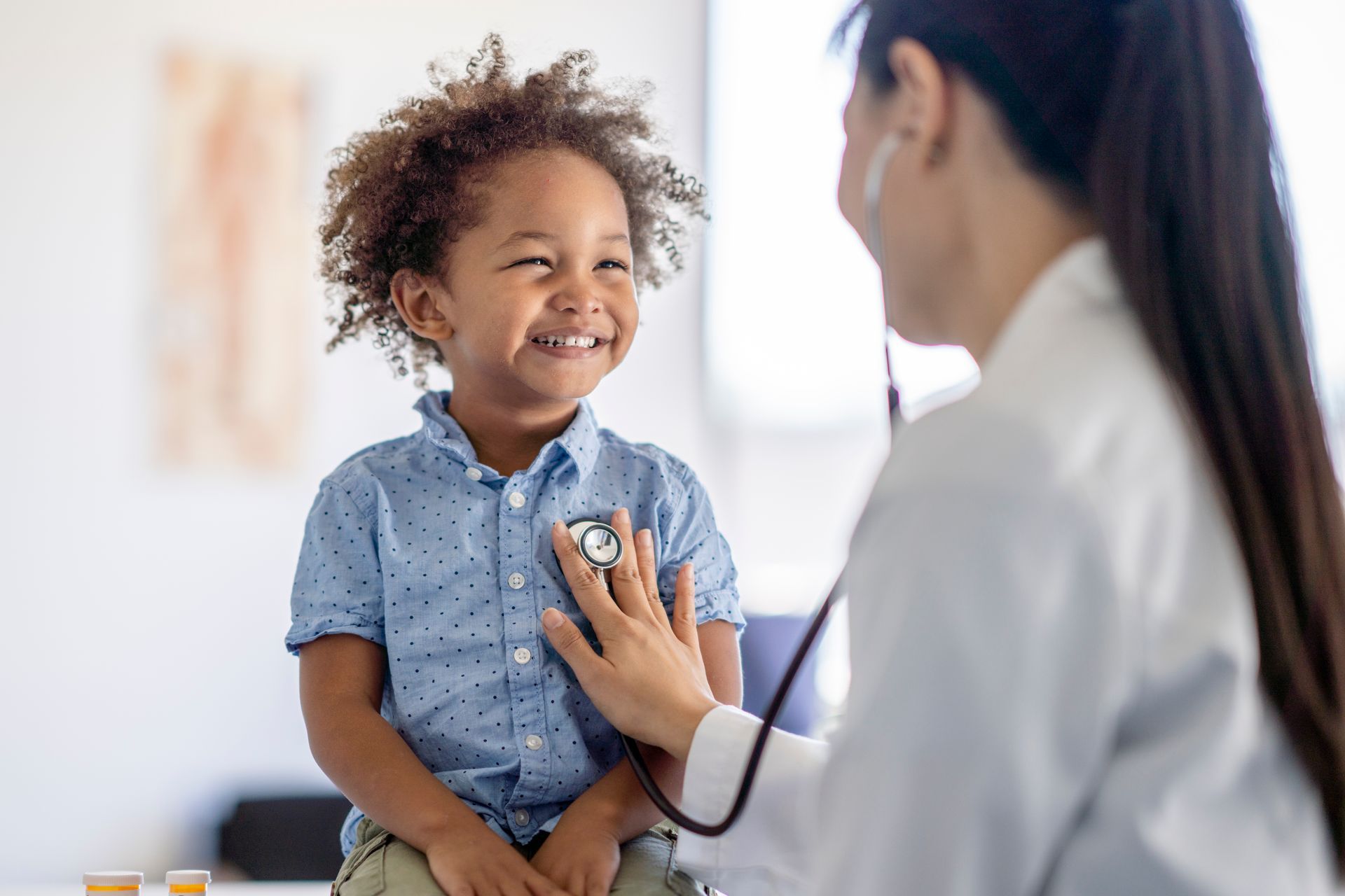 A pediatrician is listening to a smiling boy's heart