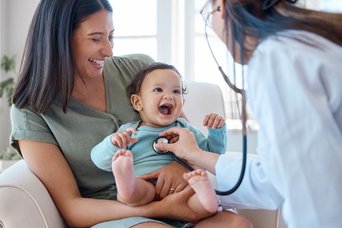 A mother is holding a laughing baby while a pediatrician examines her